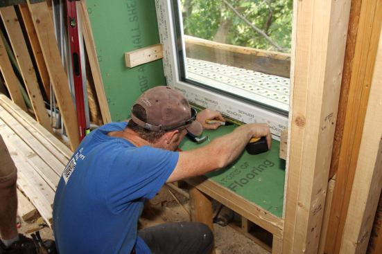 The temporary 2x3 rails and blocks hold the window in plane while the crew fine-tunes the window's placement. First, the window is roughly centered at the head jamb with shims, then it's precisely centered at the sill by measuring off the window buck.