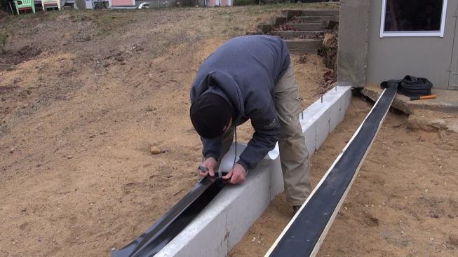 Contractor Mike Horgan installs a PVC vapor barrier onto the concrete wall footing for the new addition. To Horgan’s left we see the underside of the sill plate, with the flexible gasket already stapled onto the 2x6.