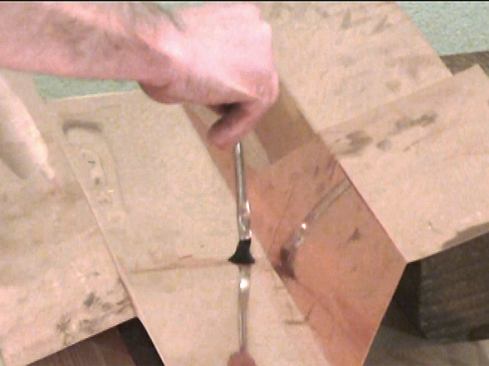 On this mock-up of the gutter liner, I’ll show how to solder a lap seam. We lap the gutter sections approximately 3 inches. Starting at the trough’s bottom seam, brush flux on both sides of the seam, making sure it flows between the sheets.