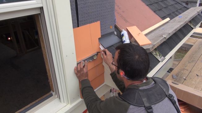 In tight quarters, Pollard uses a torpedo level to draw layout lines. The lowest five courses here are being laid out so as to have full course go over the roof head flashing.