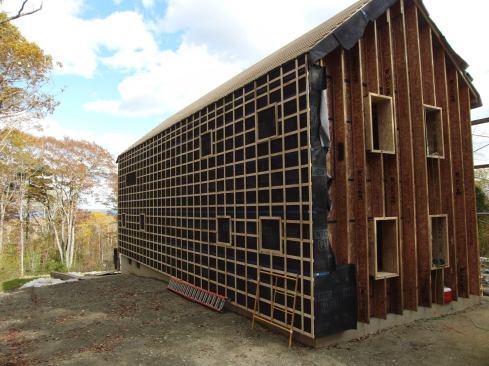 This view of a house under construction by Belfast, Maine, builder EcoCor shows one wall covered with Mento Plus fabric and criss-cross strapping, while the other wall awaits the application of the breathable drainage-plane fabric.