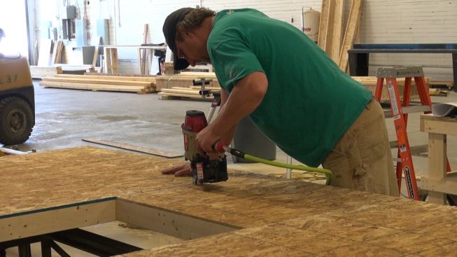 Steve Greenleaf nails OSB sheathing onto the exterior side of the interior stud frame of a Passive House wall panel. A shop table saw positioned near the wall assembly table is used to make precise sheathing cuts. Once seams are taped, the sheathing will serve as the air barrier for the house.