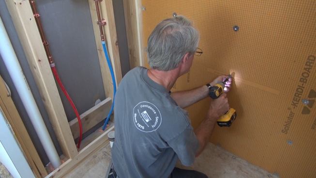 Boucher drives a screw through the washer and Kerdi-Board into the stud with a cordless impact driver.