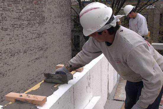 Cement mortar is applied to the poured concrete cap of the reinforced masonry parapet wall before placing the insulating foam component of an EIFS cladding for the parapet.