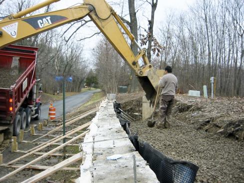 The inner face of the wall is covered with a dimpled drainage mat and the excavation is filled with stone.