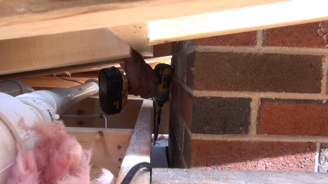 Phillips sets another screw to fasten the metal flashing securely to the ceiling framing.