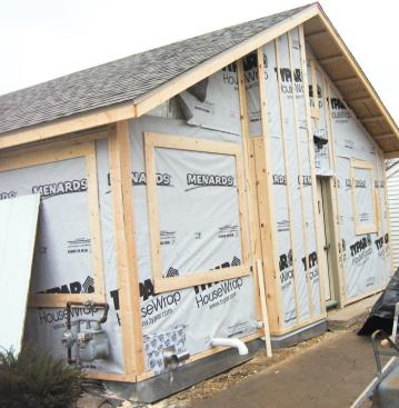 After dismantling the old gable-end chimney above the roofline, the crew enclosed the lower part in a framed, insulated bump-out. The vertical strapping over the bump-out — not yet complete on the rest of the wall — is a rain-screen nailing base for horizontal fiber-cement siding.