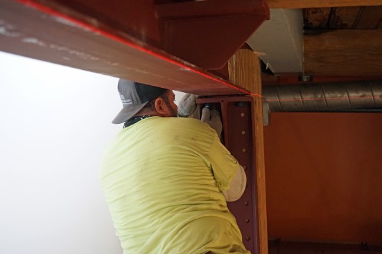 With the beam secured, a crew member lifted one end bracket into position.