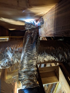 To secure the insulation, he backs out the screws on the pipe strap, pulls up the insulation, and after a final check outside to make sure the pipe is plumb and straight, he reattaches the pipe strapping permanently.