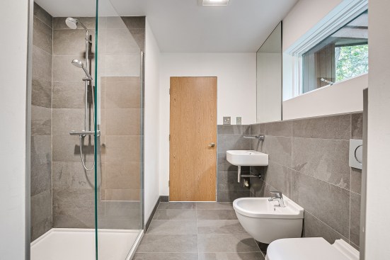 Large-format floor tiles reduce the number of grout lines, helping the space feel uncluttered. The tiles have nonslip surfaces for safety. Note the lack of trim around the door: Drywall returns in this and the other baths add to a clean, modern look.
