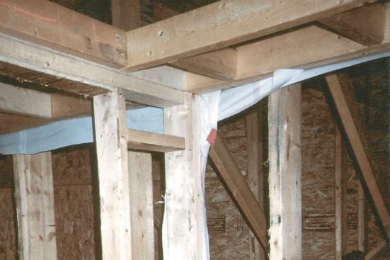 In homes where the ceiling poly can’t be installed in a single sheet, it’s installed room by room. When building the top-floor partitions, the framers must install a strip of poly between the top plates and the ceiling joists. Later, the ceiling poly in each room will be taped to the perimeter flaps