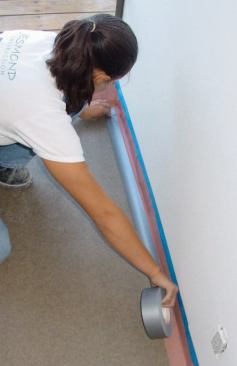 Once the rosin-paper border has been fastened to the wall with blue tape, sheets of 1/4-inch hardboard are laid over the existing flooring and attached to the rosin paper with duct tape.
