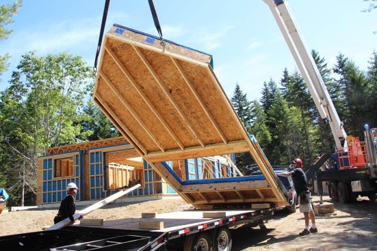 The crane lifts the largest gable end-panel off the trailer.