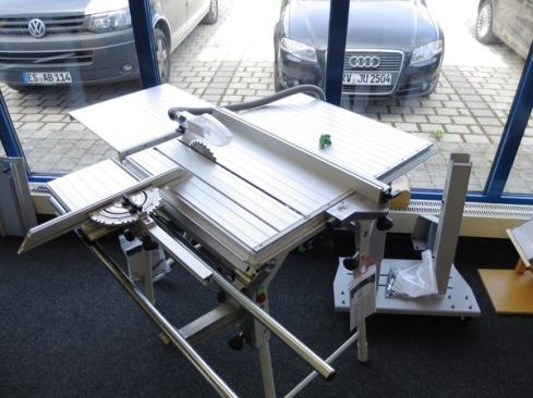 A Festool Precisio 70 table saw with an outfeed support and a sliding table. The protractor-like mechanism on the sliding table allows for precise cross-cutting at the angle of your choosing. The long slot in front of the blade is there so the blade can slide forward for cross-cutting. Note the lack of conventional blade guard. The riving knife and dust collection port on the guard above the blade—is the standard setup on European saws.