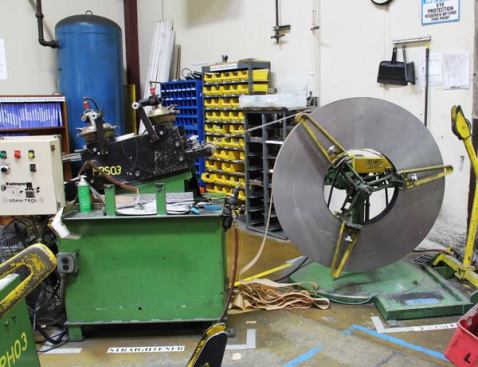 The black machine is pulling steel off of the coil and feeding it into a punch press that is off to the left. Similar setups can be seen all over the factory with different kinds of punch presses.