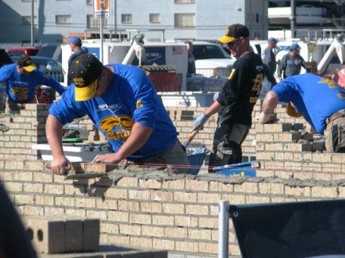 Masons and tenders hard at work in the Bricklayer 500 contest. The mason who lays the most brick in an hour wins.