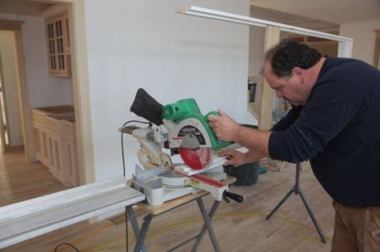 Step one of the zoom bracket is wide open showing the carpenter and the saw as well as the door jamb on the bench.