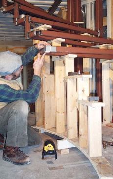 The author uses a temporary wooden stage to support tread frames while he positions them over the template. The block taped to the corner of this tread has the same cross section as a riser  bar; its center is being used as the laser target.