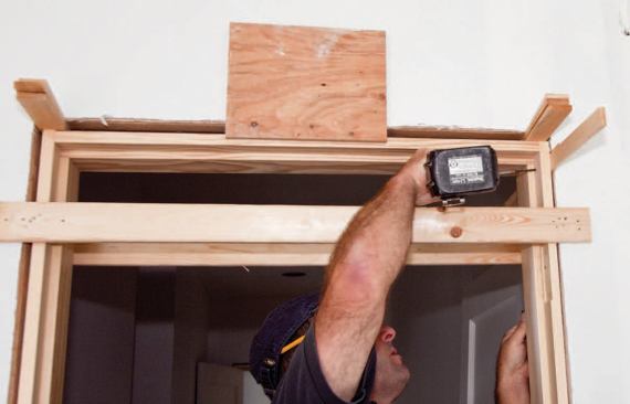 With shims at the header pinning the side jambs to the floor, the author screws the top of the hinge jamb to the framing.