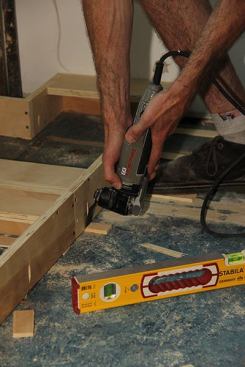 With the toe-kick base screwed firmly down, Joe buzzes off the shims flush to the base using an oscillating multi-tool.