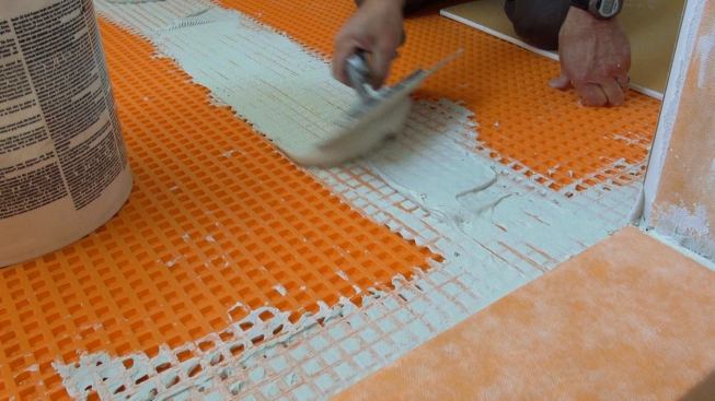 Boucher uses the notched trowel to calibrate the depth of the fresh mortar bed at a joint between two pieces of Ditra underlayment.