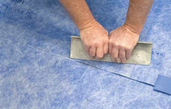 He flattens the seam with a straightedge. Sealant squeeze-out indicates the seam is closed.