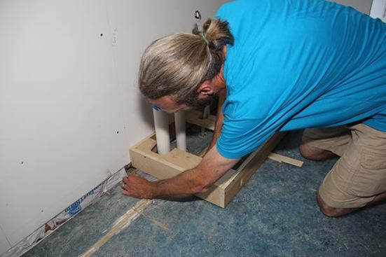 Holding the side of his pencil flat to the floor, Jeff scribes the back end of the toe-kick box to mark it for a leveling cut.