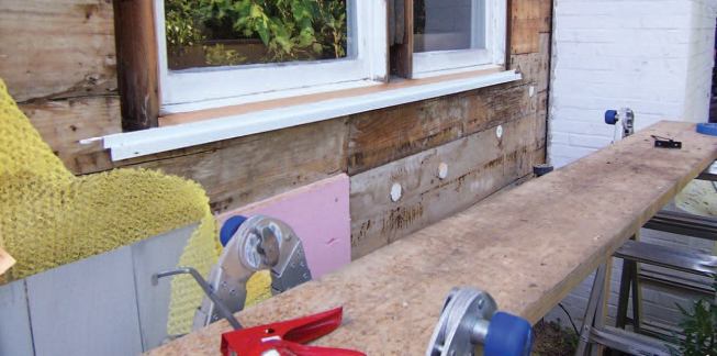 The aluminum flashings are bedded in sealant and overlap the new layer of 1-inch-thick rigid XPS foam used to wrap the house.
