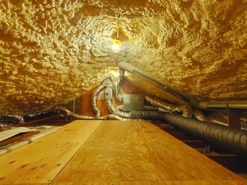 The author moved insulation from the attic floor to the roof plane, allowing mechanicals and ducting to remain inside the building envelope. First, a 1-inch air gap below the roof sheathing was created using strips of plywood as spacers and 1-inch XPS foam between the rafters topped with 12 inches of open-cell foam, for a combined R-value of around 50.