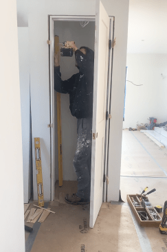 With the door hung, he aligns the latch side, keeping an even reveal (the gap between the door and the jamb). He first secures the top of the jamb. He checks to be sure the door hits the stop evenly, then secures the bottom, and finally shims behind the strike plate until the gap is correct.