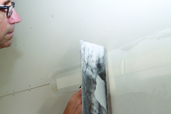 He tests the embedded tape; if it leaves a dimple, not enough mud has been forced from the back of the tape.