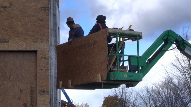 A site-improvised bracket bolted to the underside of the lift bucket helps the crew load, lift, and place the sheathing.