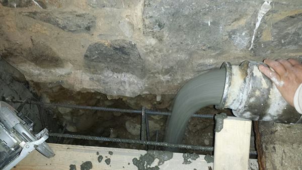 Concrete flows into the stepped forms for a reinforcing buttress. The concrete will set in contact with the existing foundation structure and undisturbed site soils, maintaining the stability of a common party wall that supports the project house as well as a neighboring dwelling.