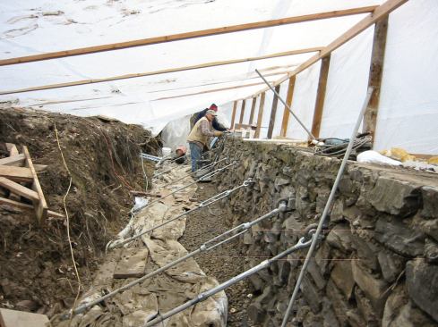 The grouted wall pins and hardware are mechanically fastened to the exposed ends of the helical soil anchors.