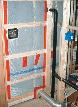 Where this dryer vent penetrates the exterior wall (at bottom of photo), a plywood block provides a surface for taping the poly air barrier. This house has horizontal wall strapping, so there was no need to recess the plywood block between the studs. Note that where the partition meets the exterior wall, the penetrations for the plumbing vent and electrical cable are sealed with urethane foam. The photo also shows an Enviroseal airtight electrical box.