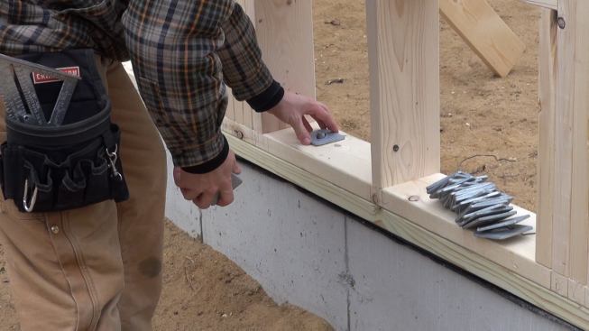 Russ Laffin sets three-inch square foundation bolt washers in place on the new wall, as required by recent versions of the building code for walls in coastal locations that may be subject to high wind forces.
