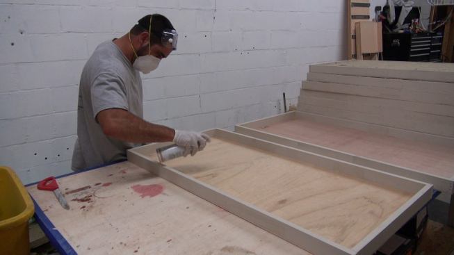 Spraying the frame’s plywood back with adhesive.