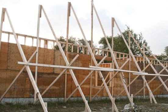 Workers framing roofs with trusses have been injured and killed by the domino-like collapse that can occur when one truss leans against the next and the whole set topples. To prevent this from happening, the author’s crew has already set up a series of vertical supports and an array of diagonal braces that run back to the ground at the gable end.