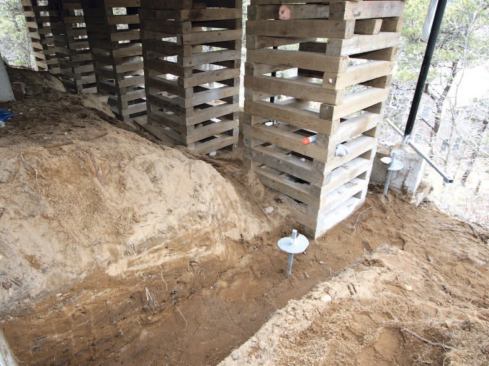 To set up jacking stations and restore the building to a level condition, the crew shoveled out a level base behind the failed grade beam and stacked cribbing under the floor joists, leaving just enough room for helical piers.