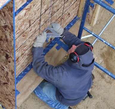 A carpenter snaps a layout line for the wood I-joist on the house wall. I-joist flanges line up with studs in the wall, and are screwed into the studs using GRK structural fasteners. The taped OSB skin on the inner stud wall serves as the airtight barrier for the building.