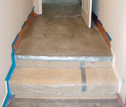 When protecting carpeted stairs with sticky roll plastic, it's important to cover the risers and full width of each tread, not just the portion that will get walked on. The landing above the steps will be covered with hardboard.