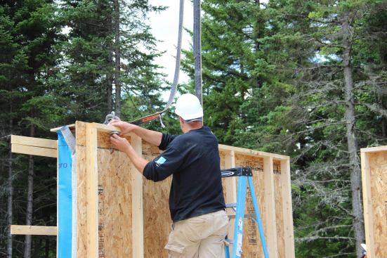 After setting a wall panel, a crew member unscrews the nut and washer from the clevice used to secure lifting straps to the panel.
