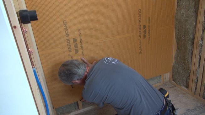 Placing the board against the wall and lifting it off the floor a few inches, Boucher marks stud locations on the board edge with a felt pen.