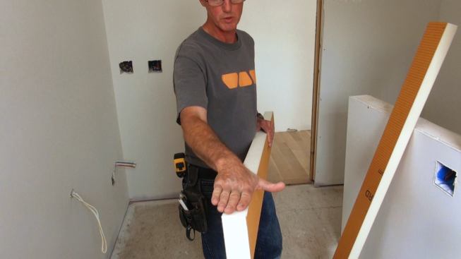 Tile contractor Tom Boucher with a two-inch-thick piece of Kerdi-Board. The board has an extruded polystyrene core and is faced with polyethylene membrane with a fleecy surface that is able to bond with mortar. Boucher has ripped the piece on a bevel, which will create a slope for drainage when the shower curb is topped with a piece of marble.