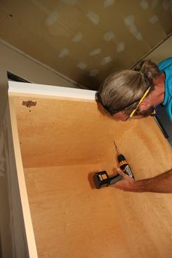 Jeff screws through the inside of the cabinet and the cleats into the end panel, securely attaching the cabinet to the panel.