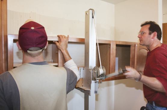The author thought out every step of the process of renovating 50 kitchens in a multi-unit seniors housing facility and provided his crew with every possible time-saving measure; labor-saving was the key to turning a profit on this tightly managed government project. Here the cabinet installers are working with a cabinet lift, which enabled them to preassemble banks of wall cabinets in a staging area, then wheel them into the kitchen and fasten them in place in a single step.
