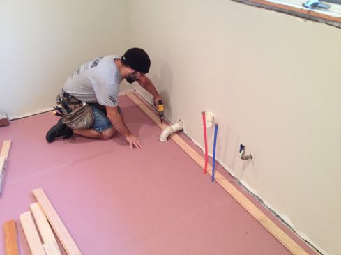 When the exact position of the starter strip has been determined, Manny pre-drills and drives screws through the face to hold it in place. The screws anchor the starter strip more solidly than nails would to keep it from moving as subsequent courses are nailed against it. All courses must be attached by hand until there is enough space for the floor nailer to be used.