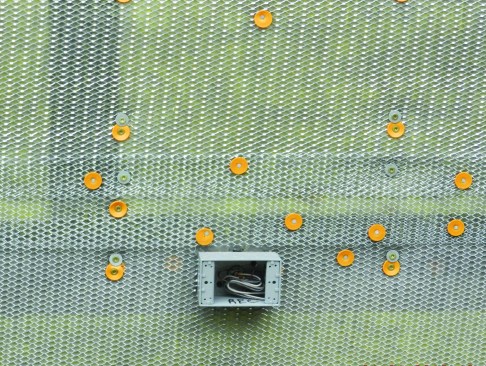 Since the lath carries the full weight of the mortar scratch coat and the thin-stone veneer, the carpetry crew secured the lath every 6 inches vertically along the studs with 4 1/2-inch HeadLok screws (with grey washers). This fastener specification for securing cladding through foam, for a cladding weight of 25 pounds per square foot, came from the FastenMaster Technical Evaluation Report (TER 1009-01) for HeadLok screws.