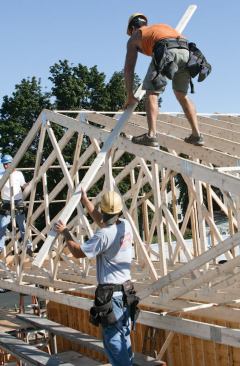 Also at midlevel, in the center of the truss span, a carpenter works from the rolling staging, installing spacers and bracing on the lower truss chords and helping to pass material to the carpenters assigned to work at the top of the trusses.