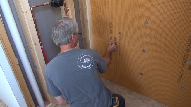 Using pre-printed lines in the Kerdi-Board as a guide, Boucher positions his washers at one-foot spacing along the stud layout lines.